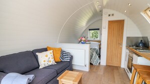 A cozy interior with a grey sofa, a small wooden table, and a kitchen area with a window and a door. - Ash (Saltash)