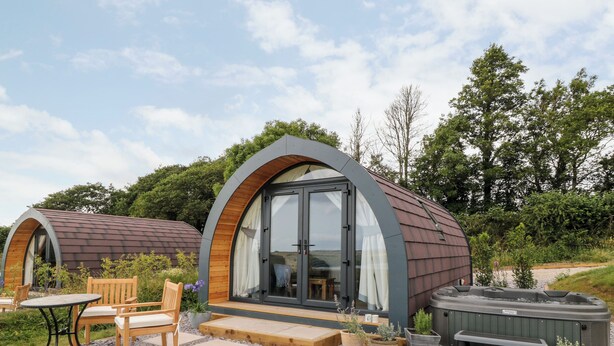 A modern, curved-roofed structure with a glass door and windows, surrounded by outdoor seating and potted plants. - Ash (Saltash)