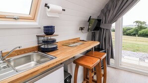 A modern kitchen with a wooden countertop, a sink, a dish rack, and a television mounted on the wall. - Ash (Saltash)