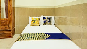 A single bed with a blue and yellow patterned bedspread, two pillows with geometric designs, and a wooden wardrobe in a corner. - OYO Life  92393 Namimart Syariah 1 (Kediri)