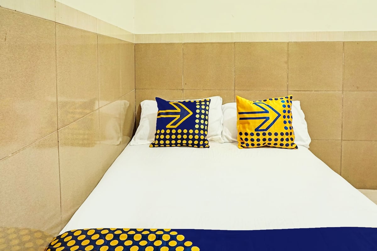 A bed with white bedding and two pillows with blue and yellow patterns.