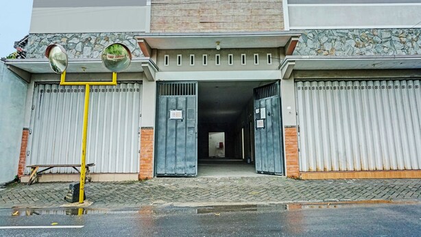 A building with a gated entrance, a yellow pole, and a stone wall. - OYO Life  92393 Namimart Syariah 1 (Kediri)
