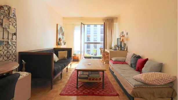 Een woonkamer met een bank, een salontafel, en een eethoek met een tafel en stoelen. Er is een raam met uitzicht op gebouwen.