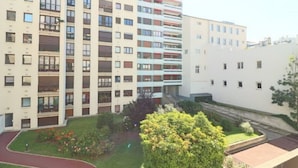 Een meerlaags woongebouw met balkons, een klein tuinpartij met een pad, en een wit gebouw ernaast.