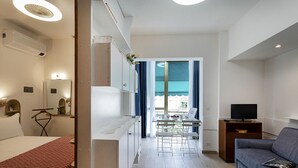 Et lille hotelværelse med seng, et lille siddeområde, tekøkken og TV.