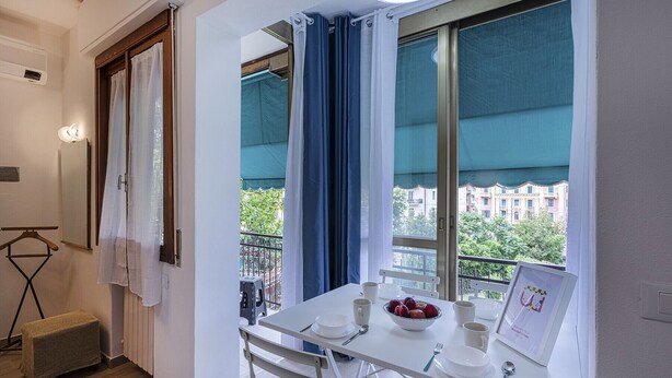 En balkon med et bord dækket til morgenmad, en stol, en lille varmeovn og udsigt til bygninger og træer.