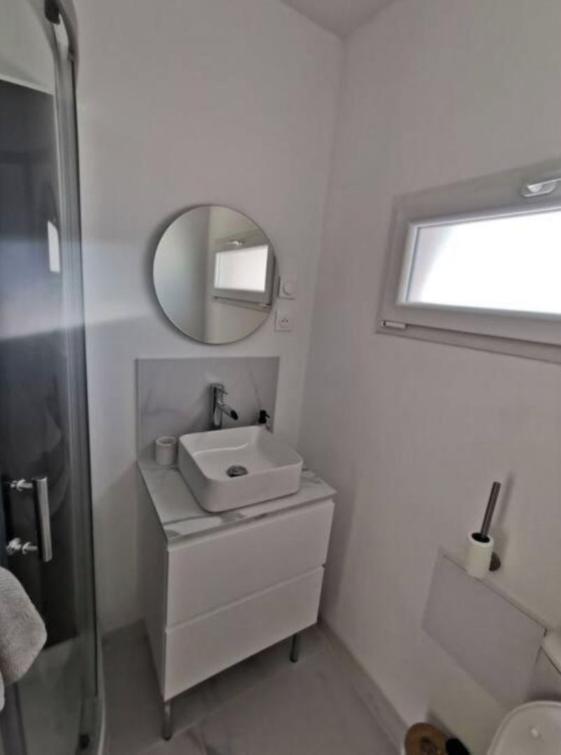Un baño pequeño y moderno con un lavabo blanco, un espejo redondo y una ventana.