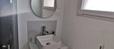 Un baño pequeño y moderno con un lavabo blanco, un espejo redondo y una ventana.