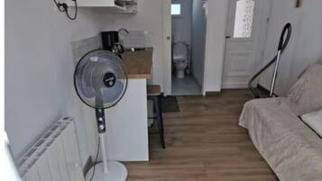 Un espace de vie compact comprenant un coin cuisine, un ventilateur, un lit et une vue sur la salle de bain.