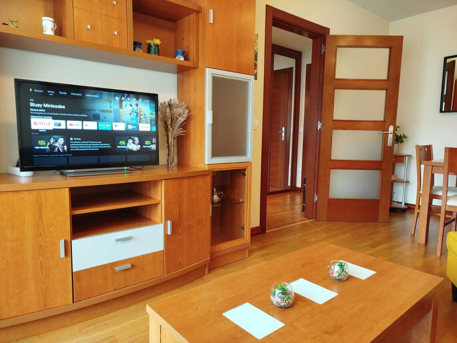 A living room with a wooden cabinet, a flat-screen TV, and a dining table with decorative items.