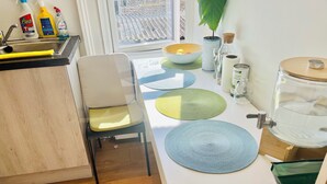 A kitchen with a sink, a chair, a bowl with fruit, a water dispenser, and a window with a view of a building. - Very Lovely and Central 1-bed Apartment in London (London)