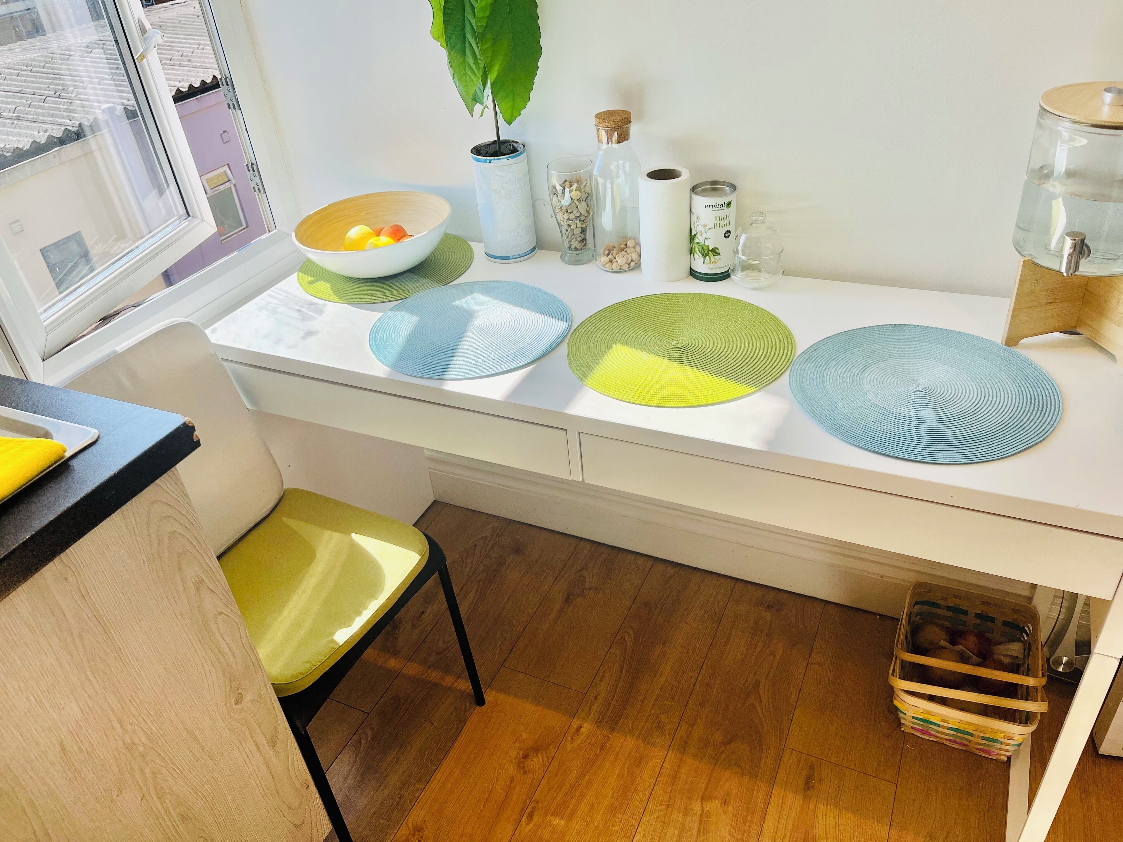 A kitchen with a white countertop, a bowl of fruit, a potted plant, and a water dispenser.