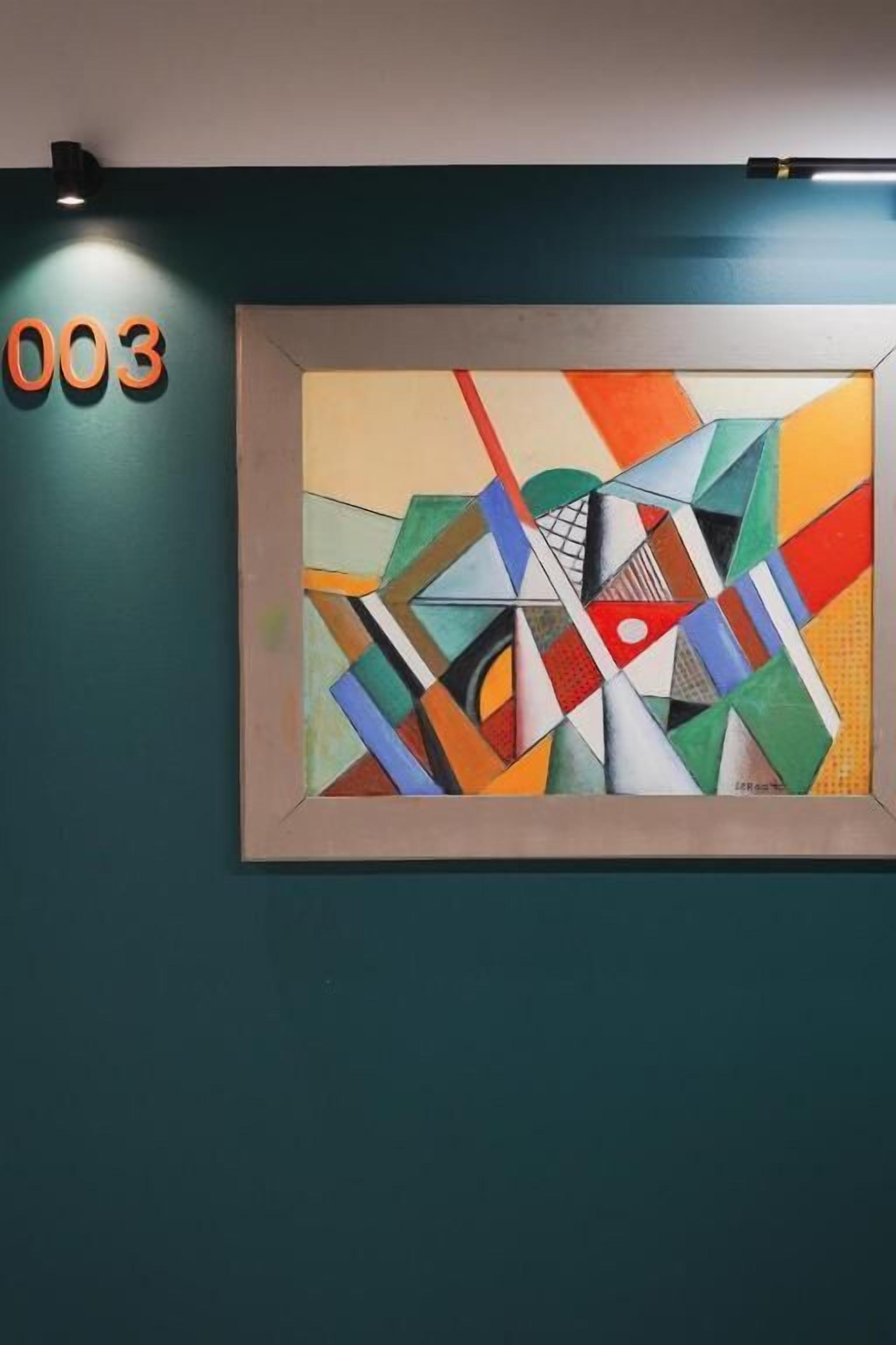 Ein gerahmtes, abstraktes Gemälde an einer taubenfarbenen Wand, oberhalb davon die Nummer '003'.