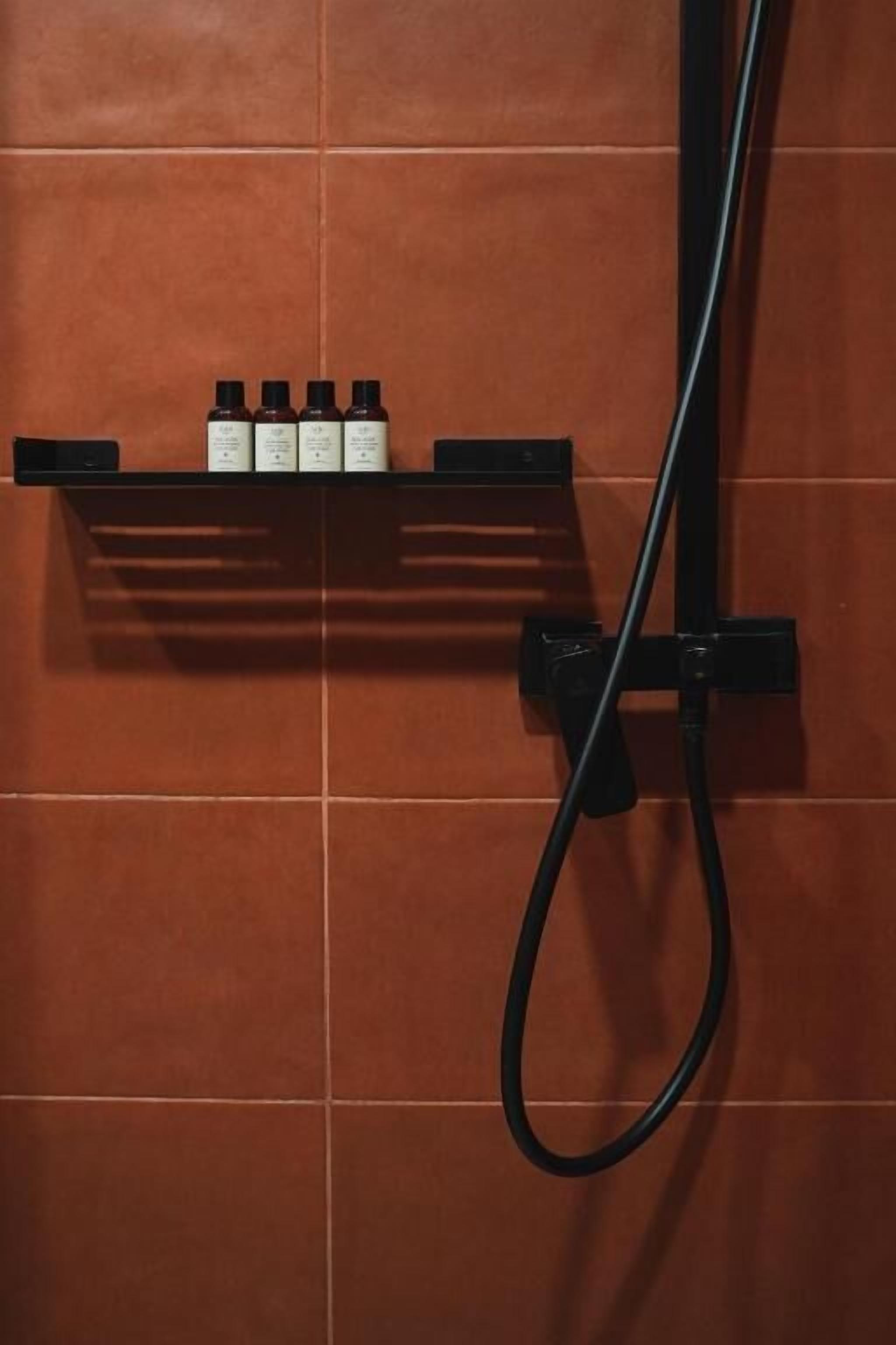 A bathroom with a shower head and a shelf with three bottles.