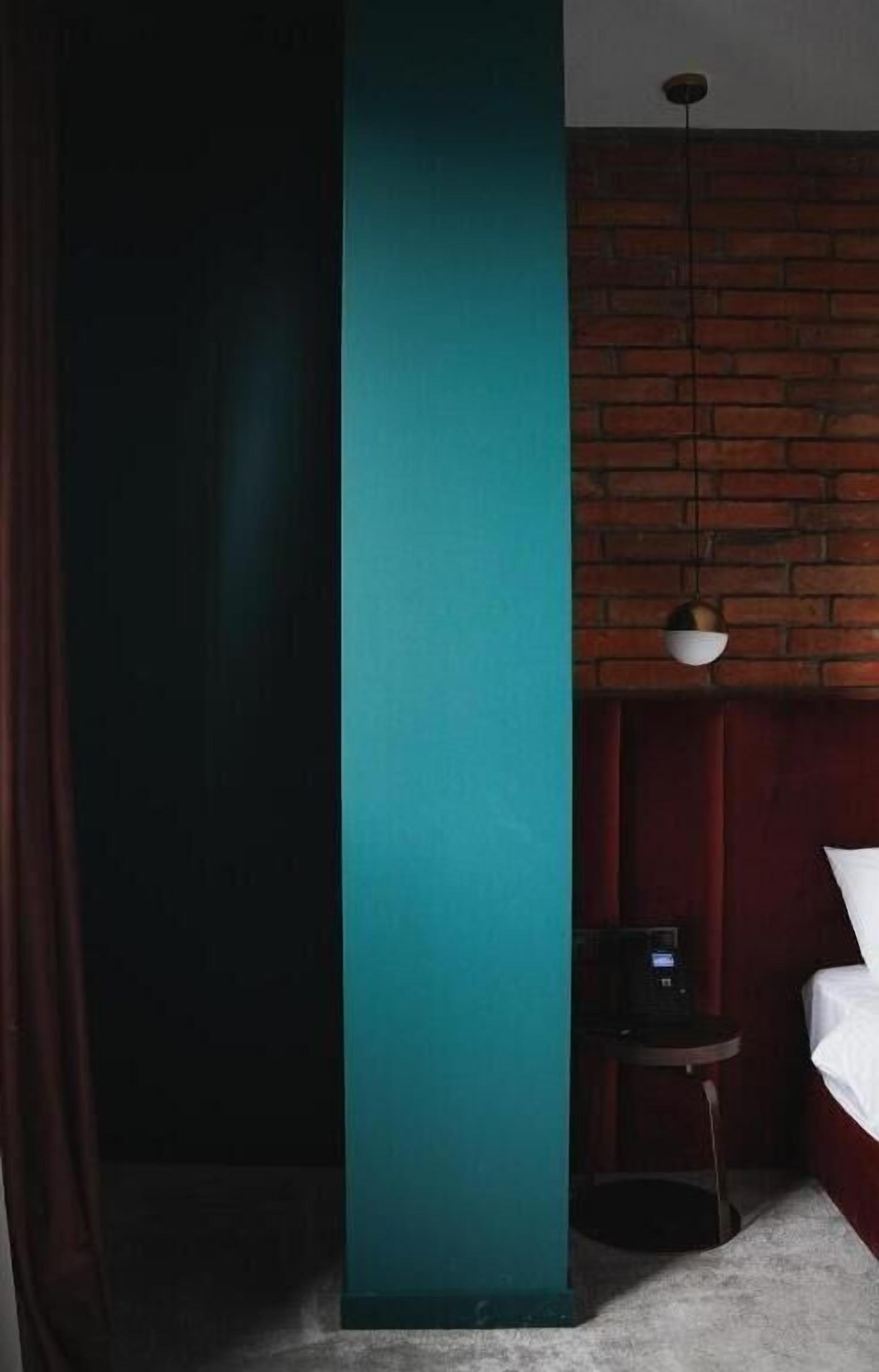 A hotel room with a teal accent wall, a brick wall, a small table with a coffee maker, and a hanging light fixture.