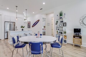 Une cuisine moderne avec des meubles blancs, un réfrigérateur en acier inoxydable et une table de salle à manger ronde entourée de chaises bleues.