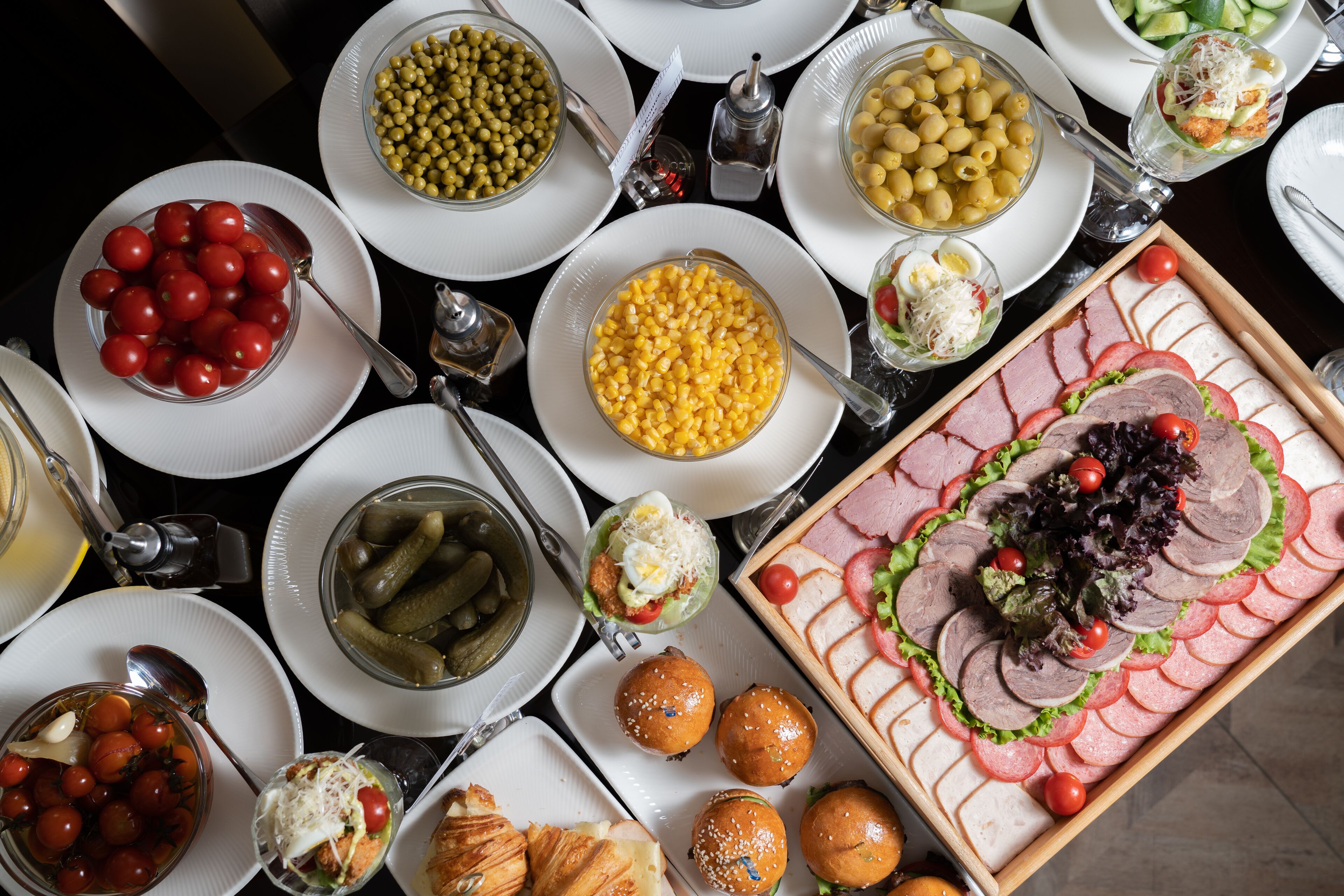 Uma mesa com diversos alimentos, incluindo tomates, milho, azeitonas e sanduíches.