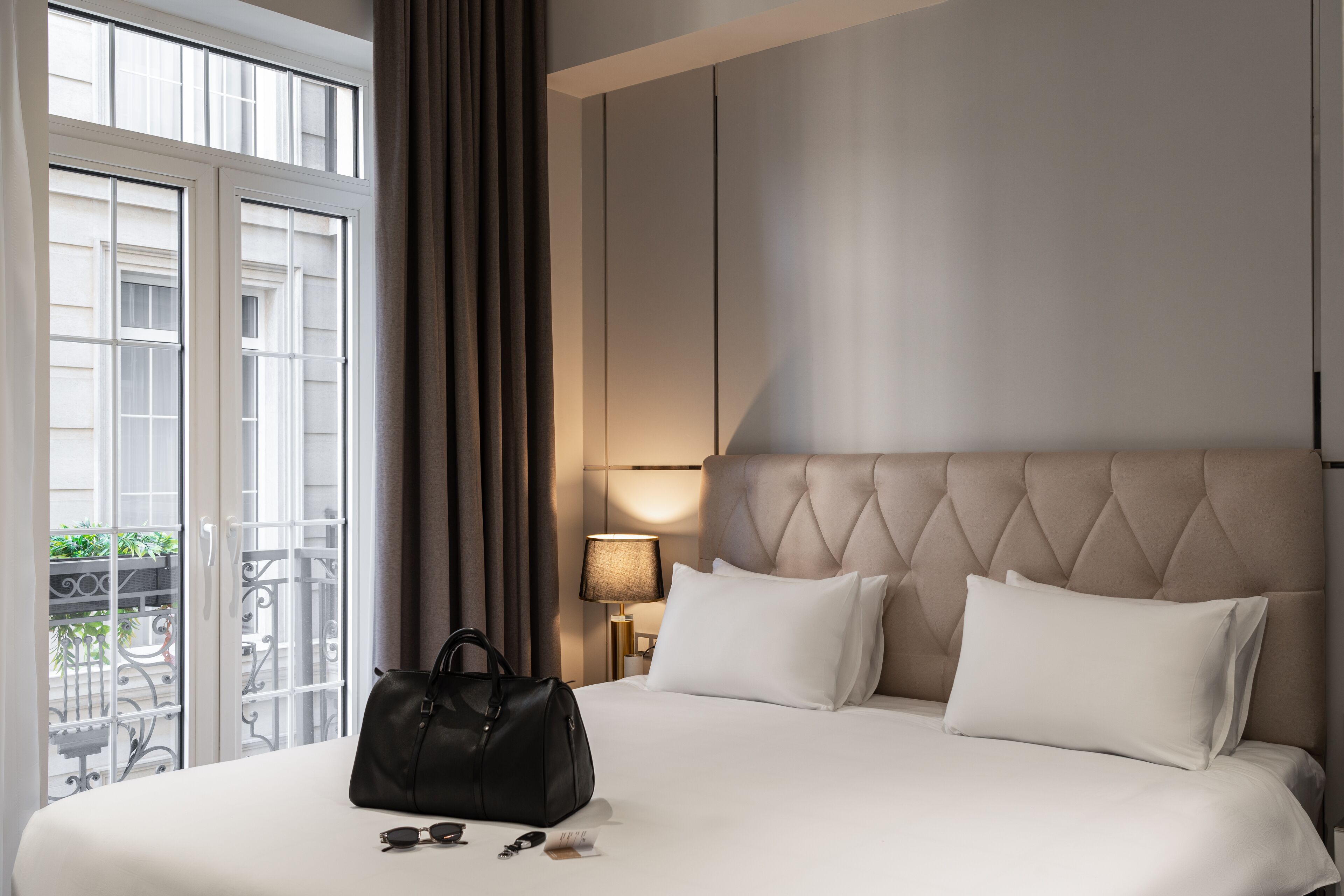 A hotel room with a large bed, a headboard, a nightstand, a lamp, and a view of the outside balcony.