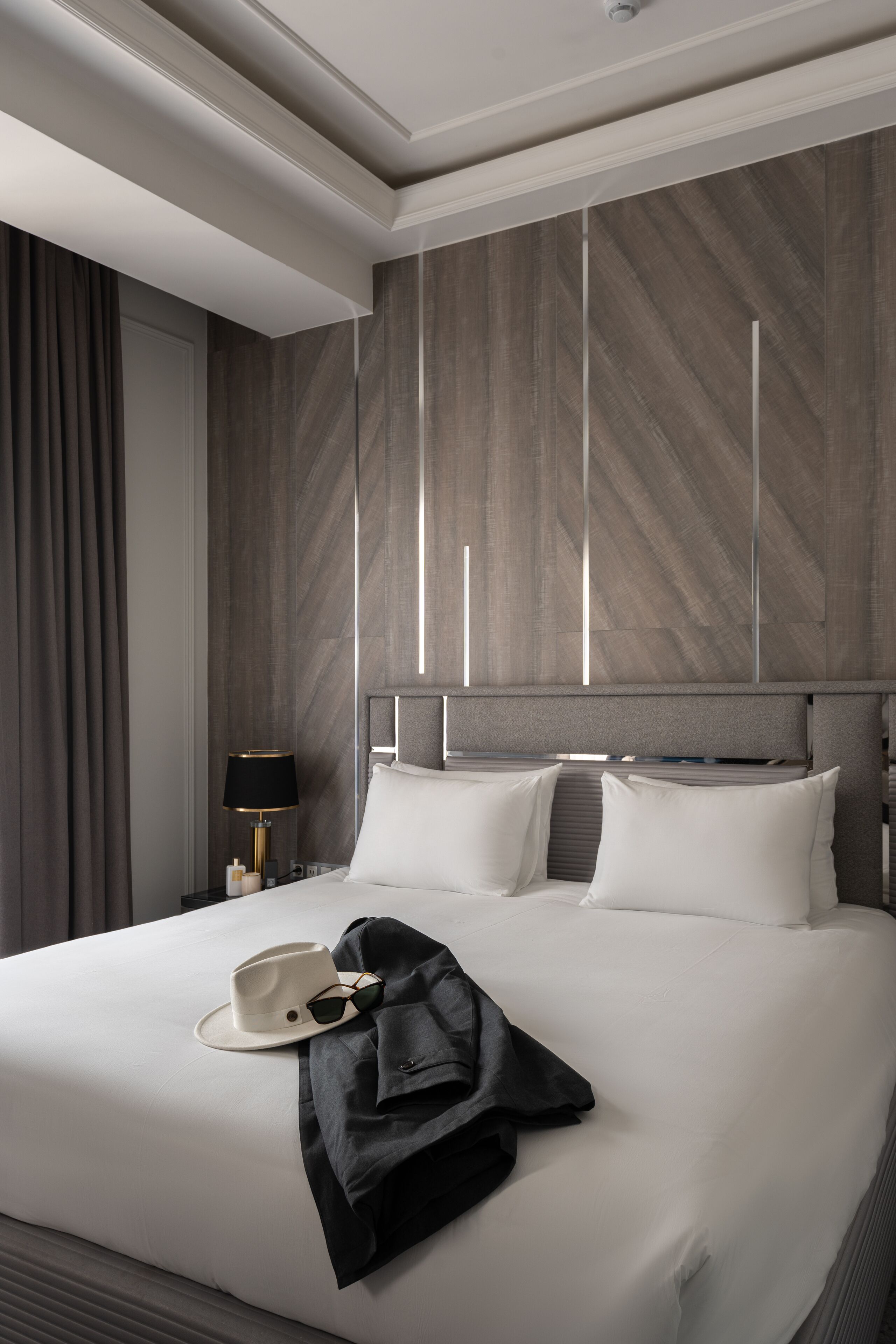 A modern hotel room with a large bed, a nightstand, a lamp, and a window with curtains.