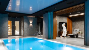 Une piscine intérieure moderne, dotée d’une eau claire, d’un escalier en métal et d’un espace de détente avec un canapé et une table.