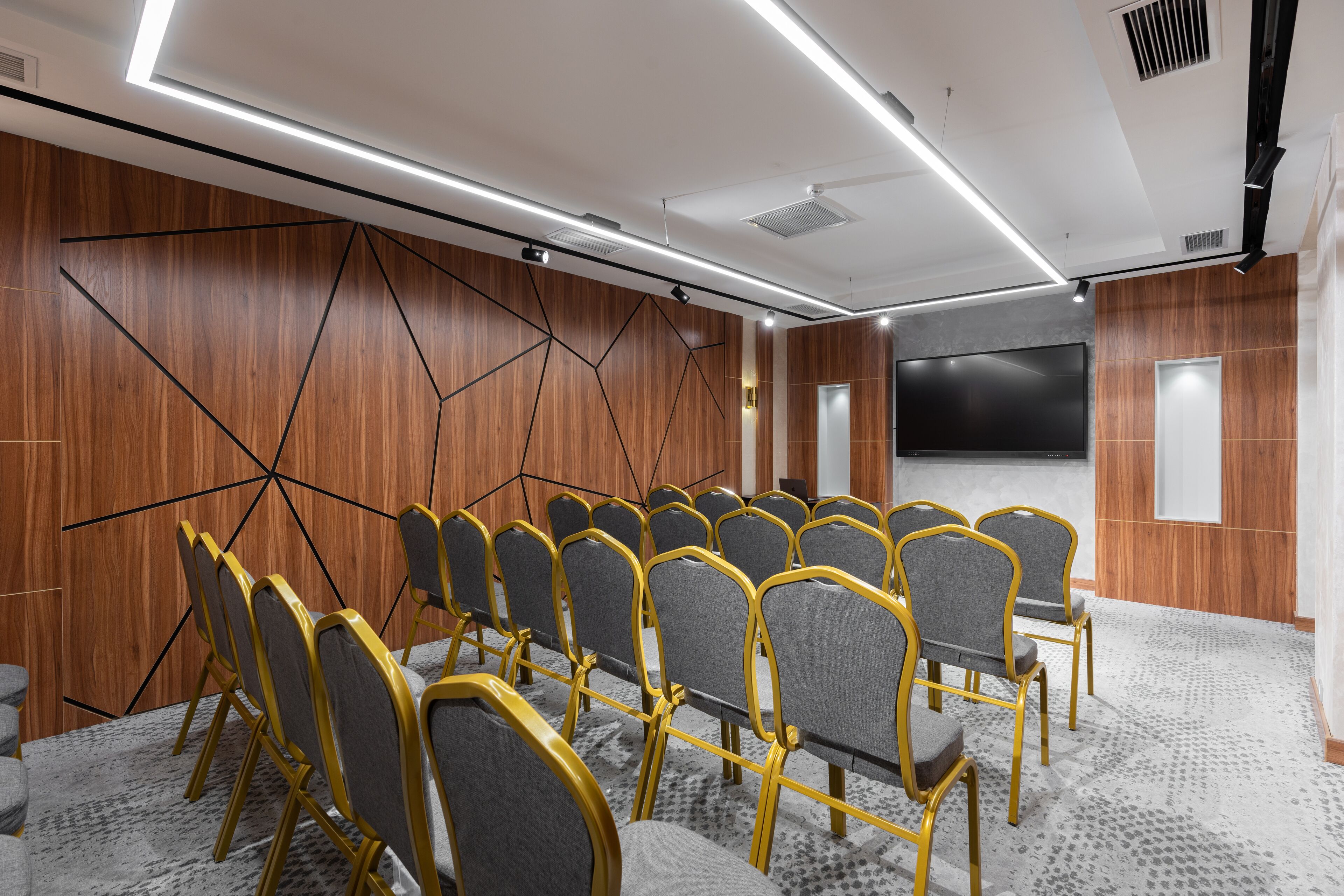 Una sala conferenze con file di sedie, un grande schermo e pannelli di legno alle pareti.
