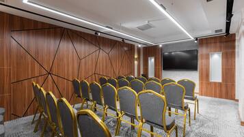 Una sala conferenze con file di sedie, un grande schermo e pannelli di legno alle pareti.