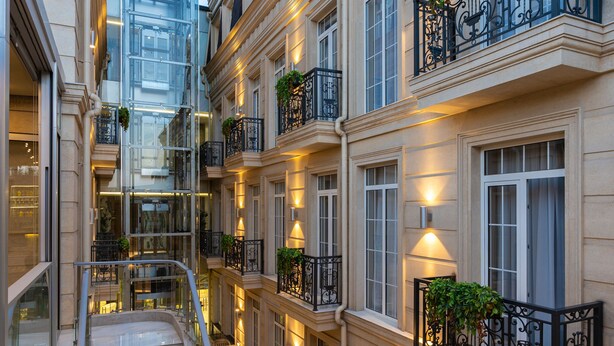 Un immeuble à plusieurs étages doté d’un escalier central, d’un espace extérieur aménagé pour s’asseoir et de balcons ornés de plantes.