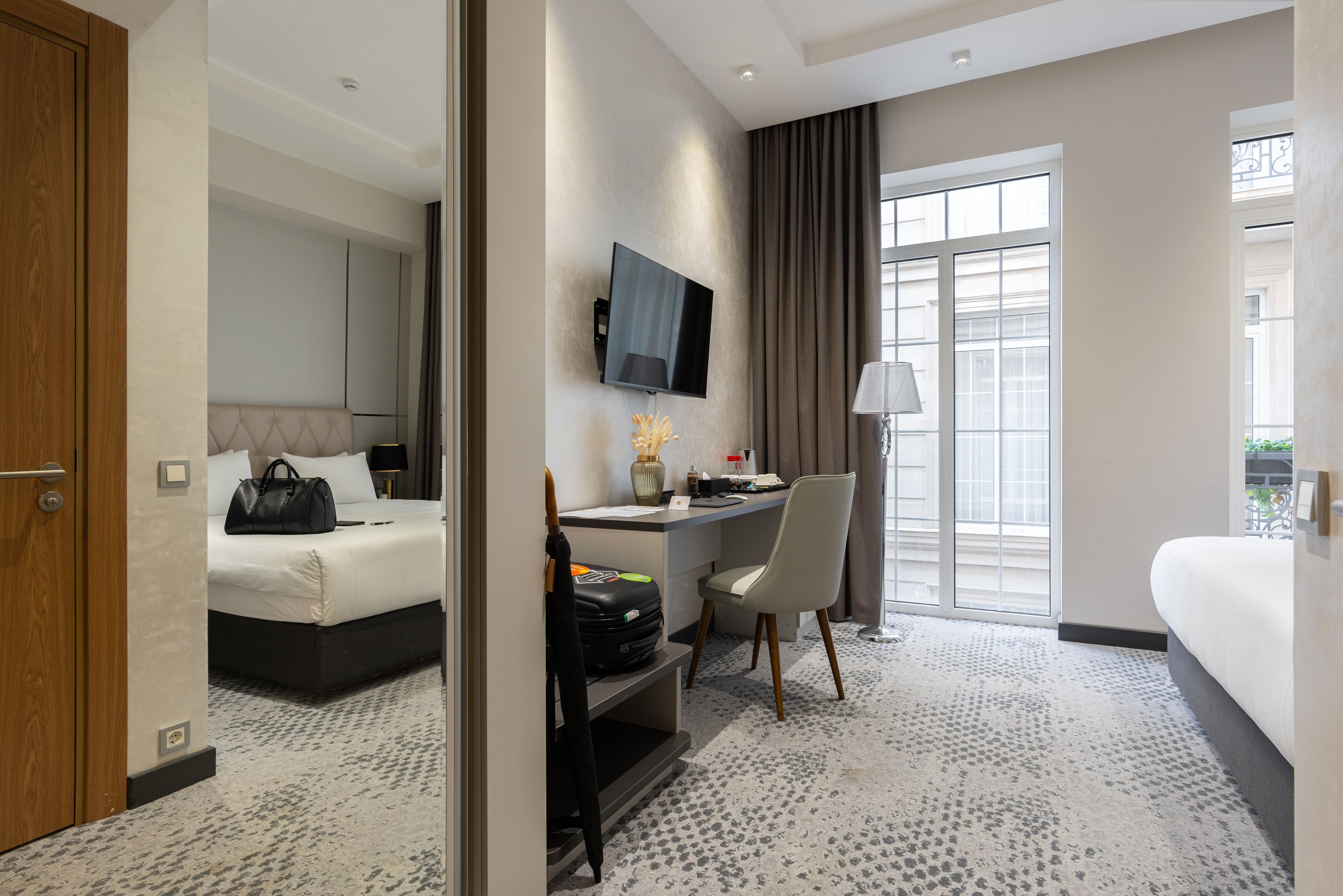 A hotel room with a bed, desk, chair, TV, and large windows.