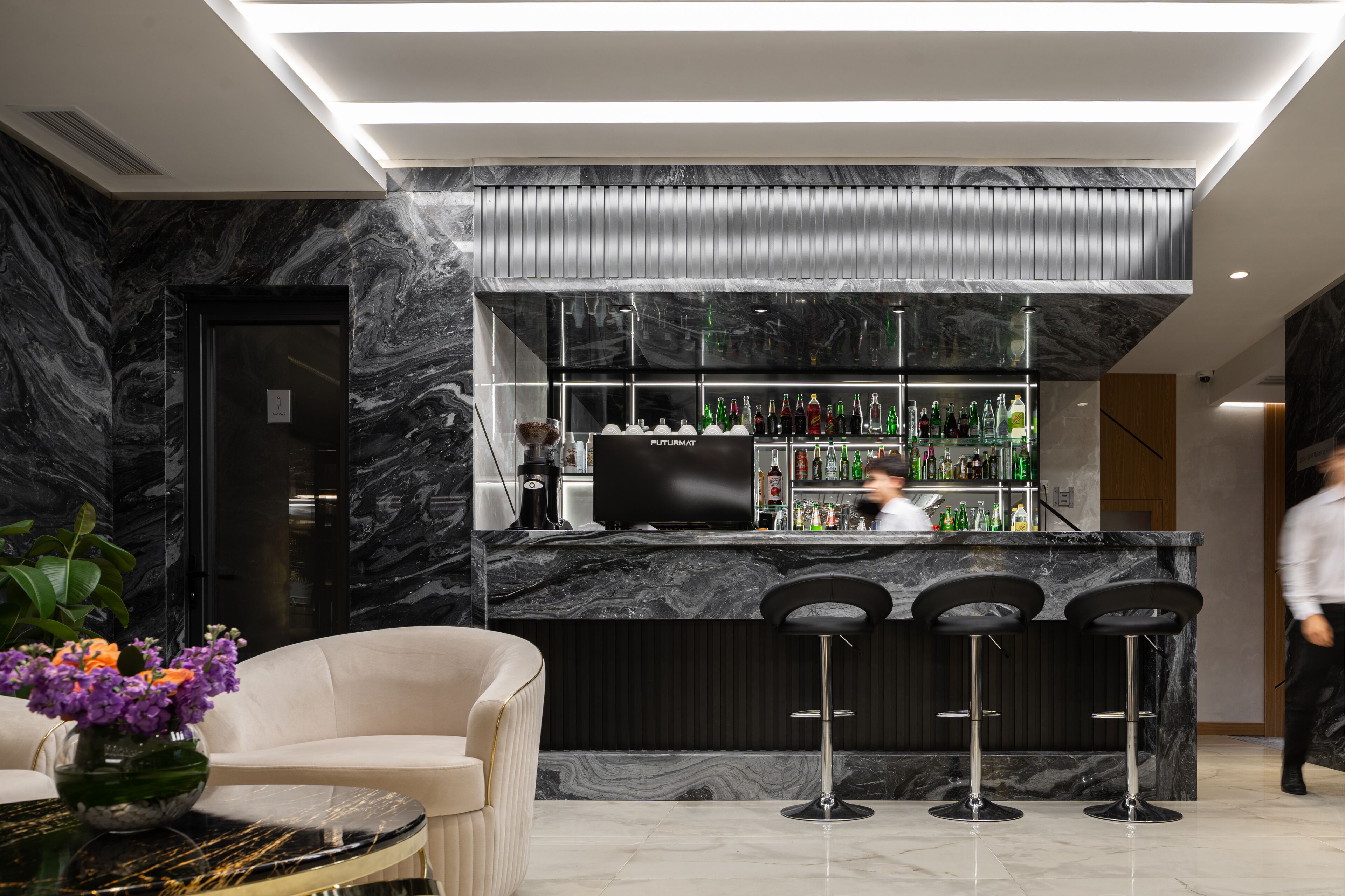 A modern bar area with marble countertops, a television, and bar stools.