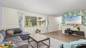 A living room with a sofa, coffee table, and a TV mounted on the wall. - Manatee & kayak friendly waterfront cottage (Ormond Beach)