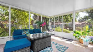 Une véranda avec un toit en verre, des meubles en osier et une vue sur un jardin.