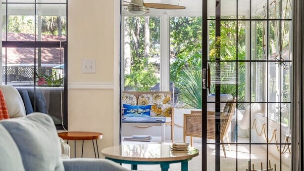 A room with a sliding glass door leading to a balcony, a ceiling fan, a sofa, a small round table, and a chair. - Manatee & kayak friendly waterfront cottage (Ormond Beach)