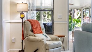 A modern living room with a beige leather recliner, a floor lamp, and a view of the outdoors through a large window. - Manatee & kayak friendly waterfront cottage (Ormond Beach)