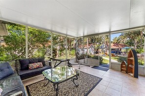 Eine überdachte Terrasse mit Glastisch, schwarzen Sitzkissen und einem Schaukelstuhl.