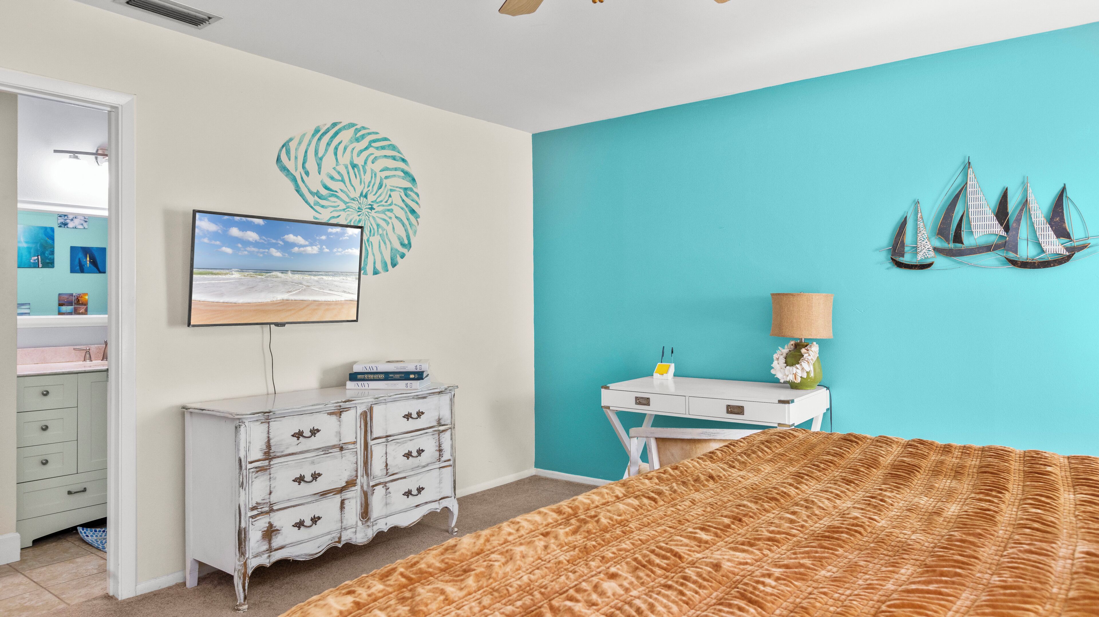 Un dormitorio con cama, tocador, escritorio, televisión y un muro con un adorno grande y decoración náutica.