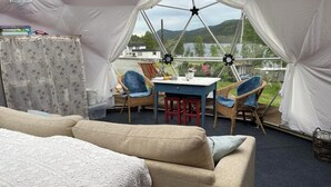 Ett mysigt tält med bekväma möbler, inklusive en soffa, stolar och ett bord, samt utsikt över en sjö och kullar.