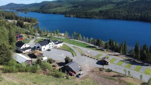 En fastighet vid en sjö med flera byggnader, en parkeringsplats och utsikt över sjön och de skogbeklädda kullarna.
