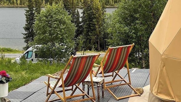 Två randiga solstolar placerade med utsikt över en sjö, med ett skogbeklätt kullområde i bakgrunden.