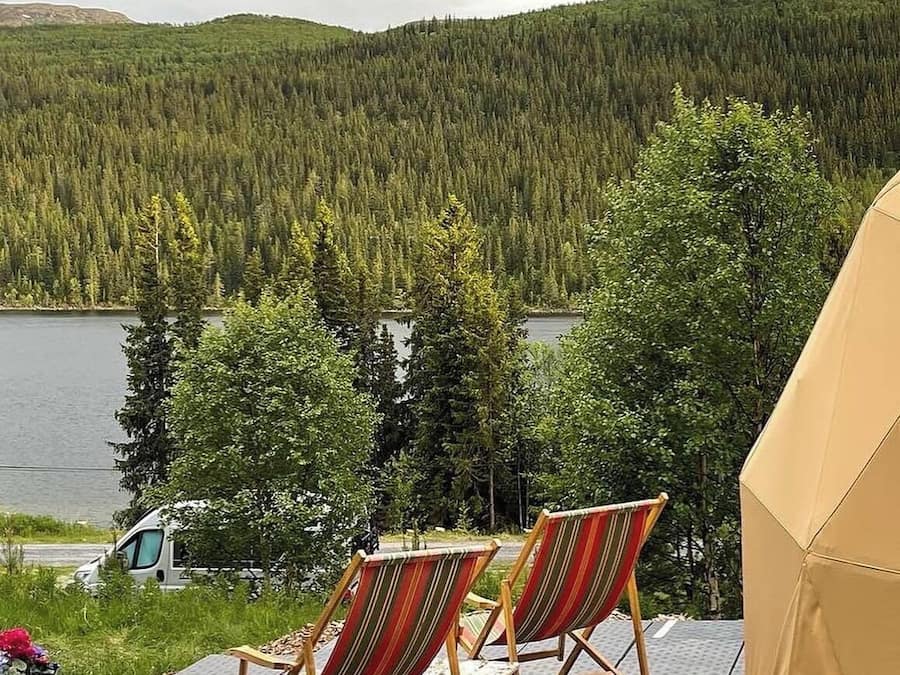 Två randiga solstolar placerade med utsikt över en sjö, med ett skogbeklätt kullområde i bakgrunden.