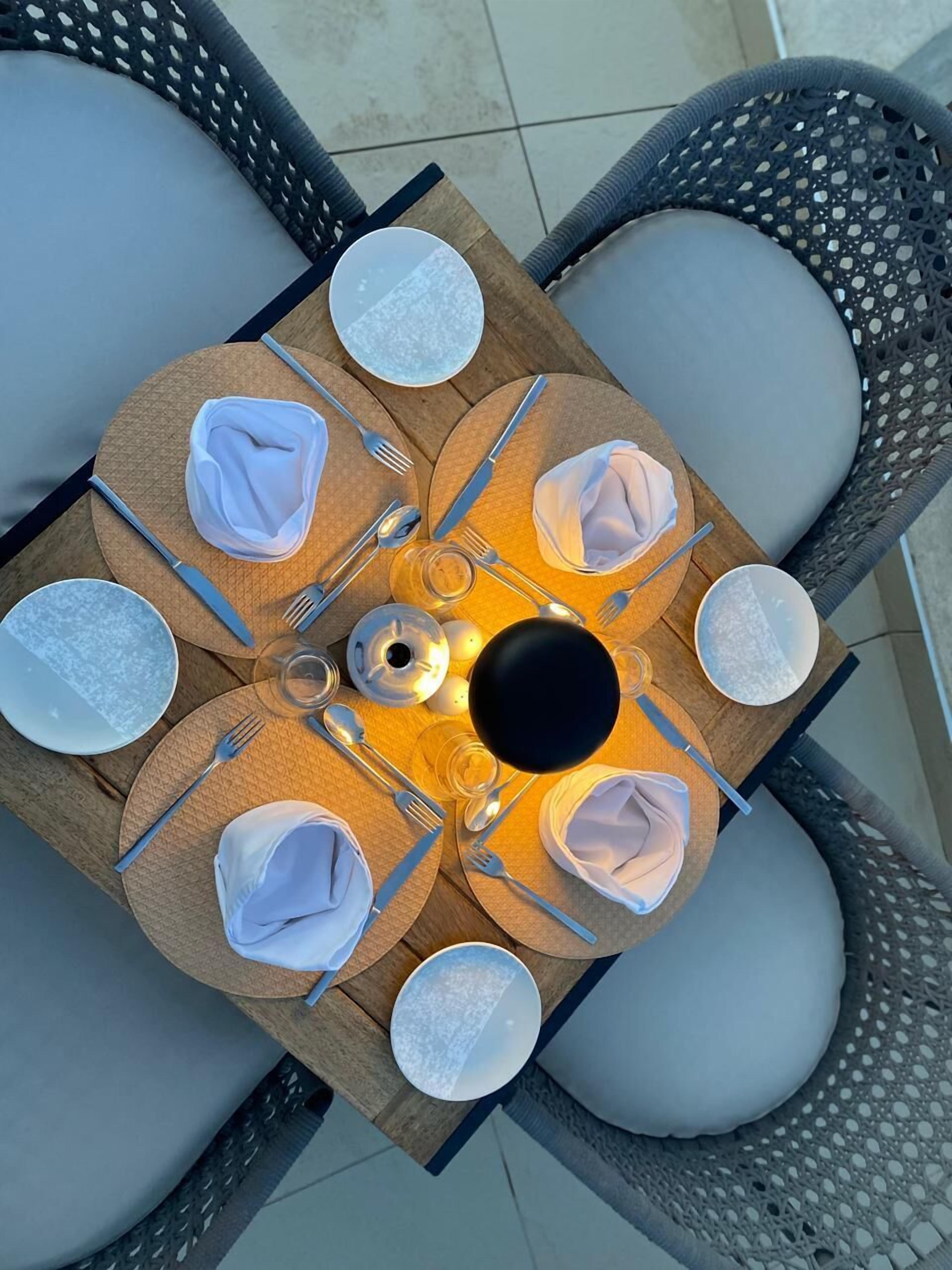 A round dining table with a central light fixture, surrounded by wicker chairs with cushions.