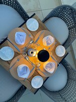 Mesa redonda de comedor con lámpara colgante en el centro, rodeada de sillas de mimbre con cojines.