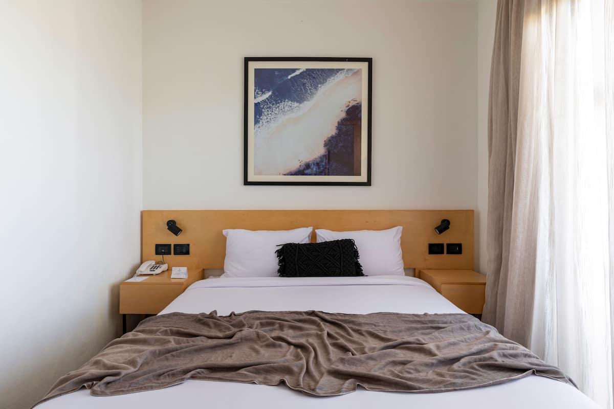 Hotellihuone, jossa on sänky, yöpöytä, puhelin ja seinällä oleva kehystetty kuva.