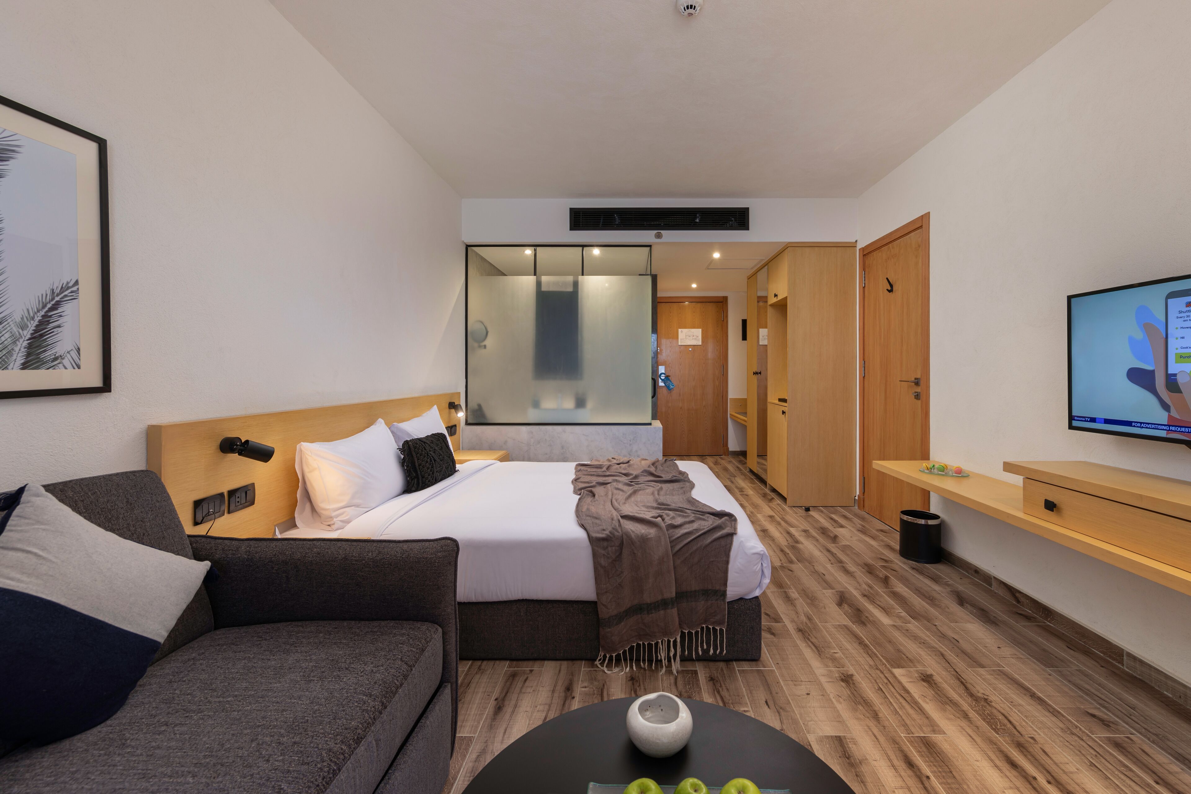 Habitación de hotel moderna con cama, sofá, televisor y suelo de madera.