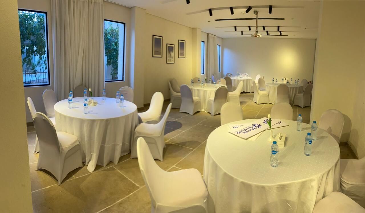 A conference room with multiple round tables, white chairs, and water bottles.