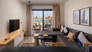 A modern living room with a flat-screen TV, a sofa, a dining table, and a view of the beach and pool. - Creek Hotel and Residences El Gouna (El Gouna)