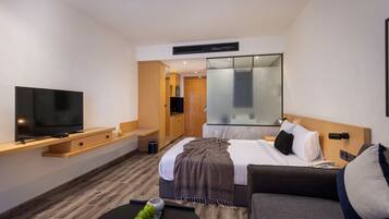 Une chambre d’hôtel moderne équipée d’une télévision à écran plat, d’un canapé, d’un lit avec une tête de lit, d’une table de chevet et d’un grand miroir.