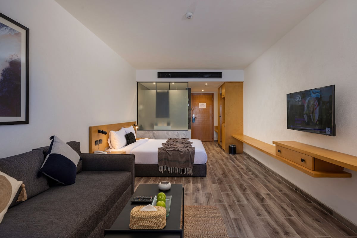 Moderni hotellihuone, jossa on sänky, sohva, sohvapöytä ja seinälle asennettu televisio.