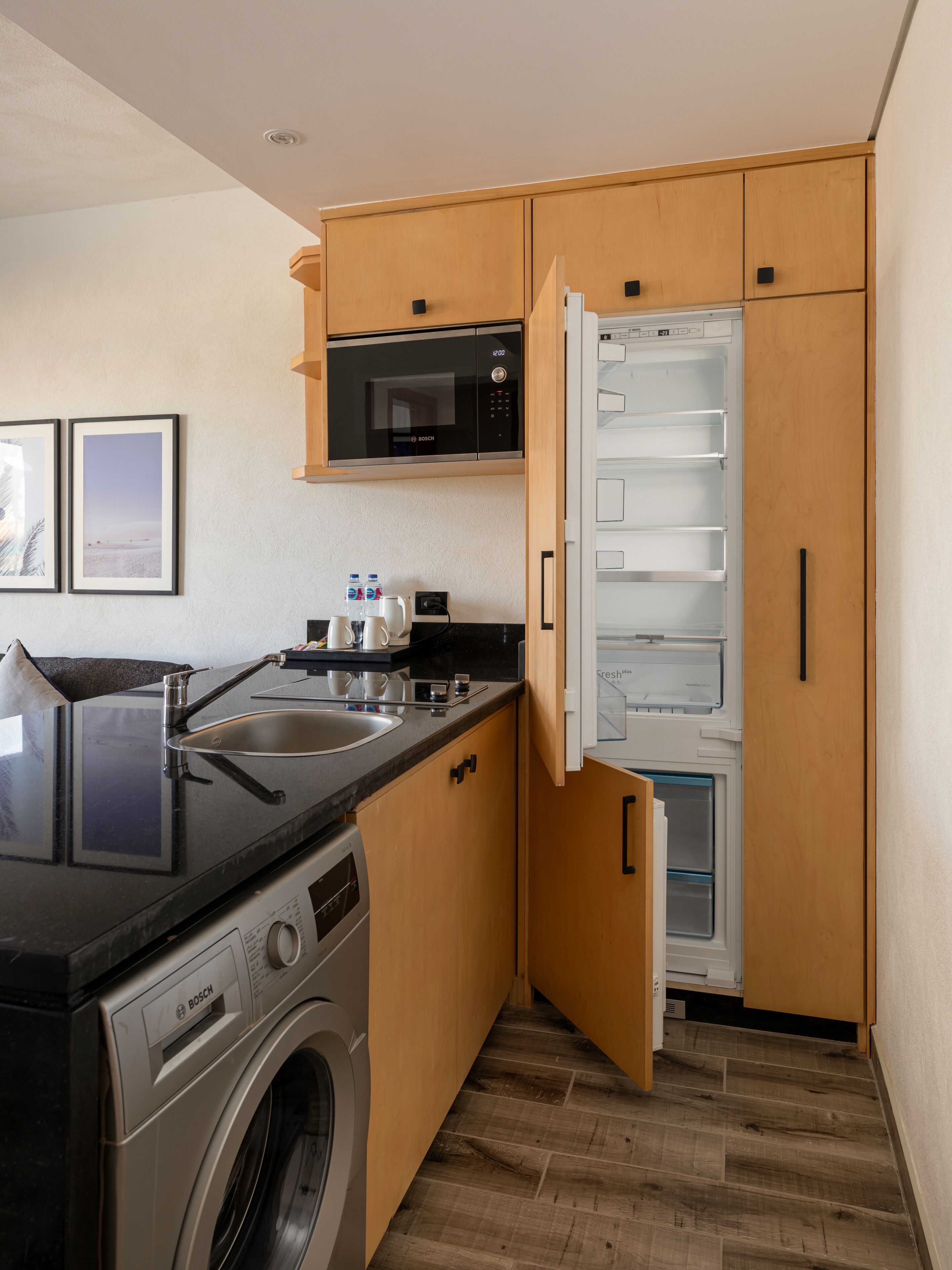 A compact kitchen with a Bosch washing machine, a microwave, and a refrigerator.