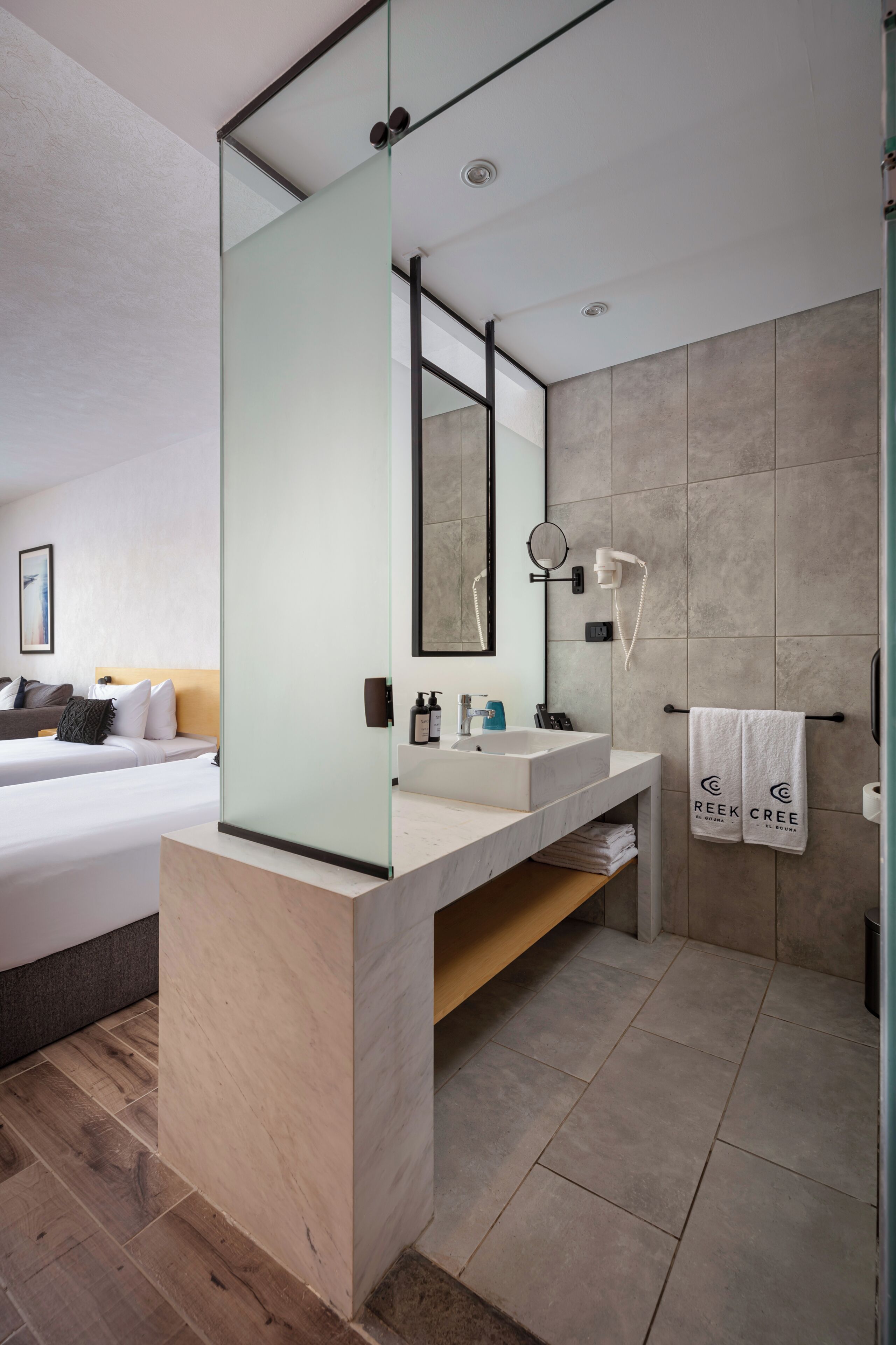 Un baño de hotel moderno con mampara de vidrio, un espejo grande, un lavamanos y una zona de ducha.