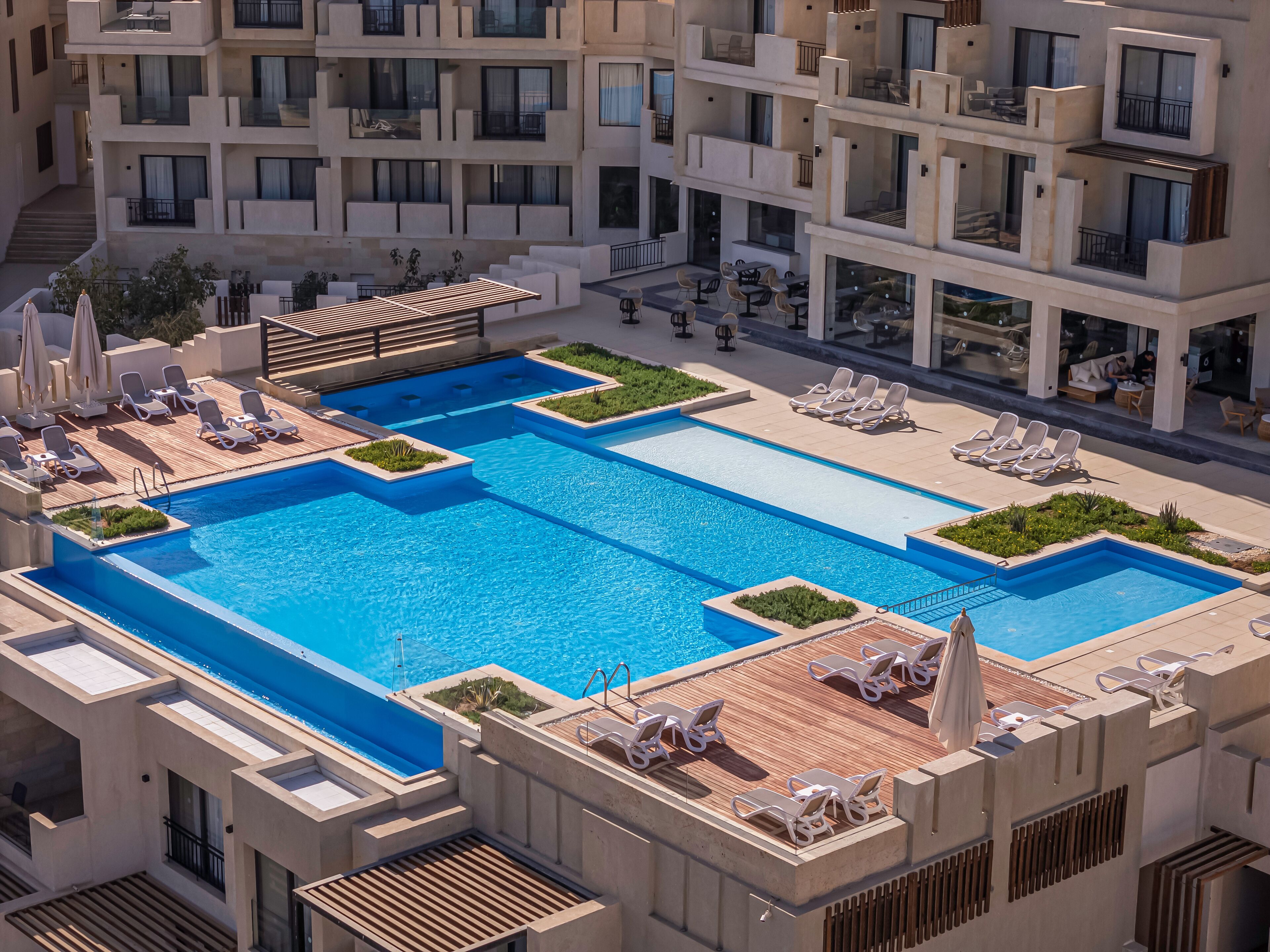 A rooftop swimming pool with multiple levels of balconies, lounge chairs, and a wooden deck area.